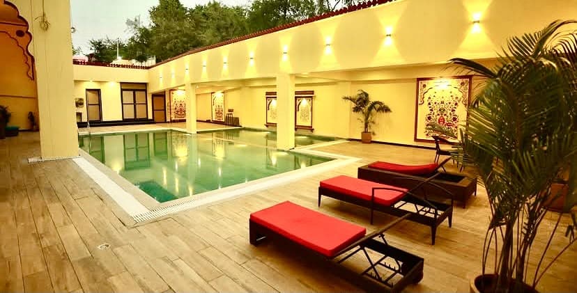 Heritage hospitality swimming pool with wooden sun deck, ambient sconce lighting and traditional floral fresco murals